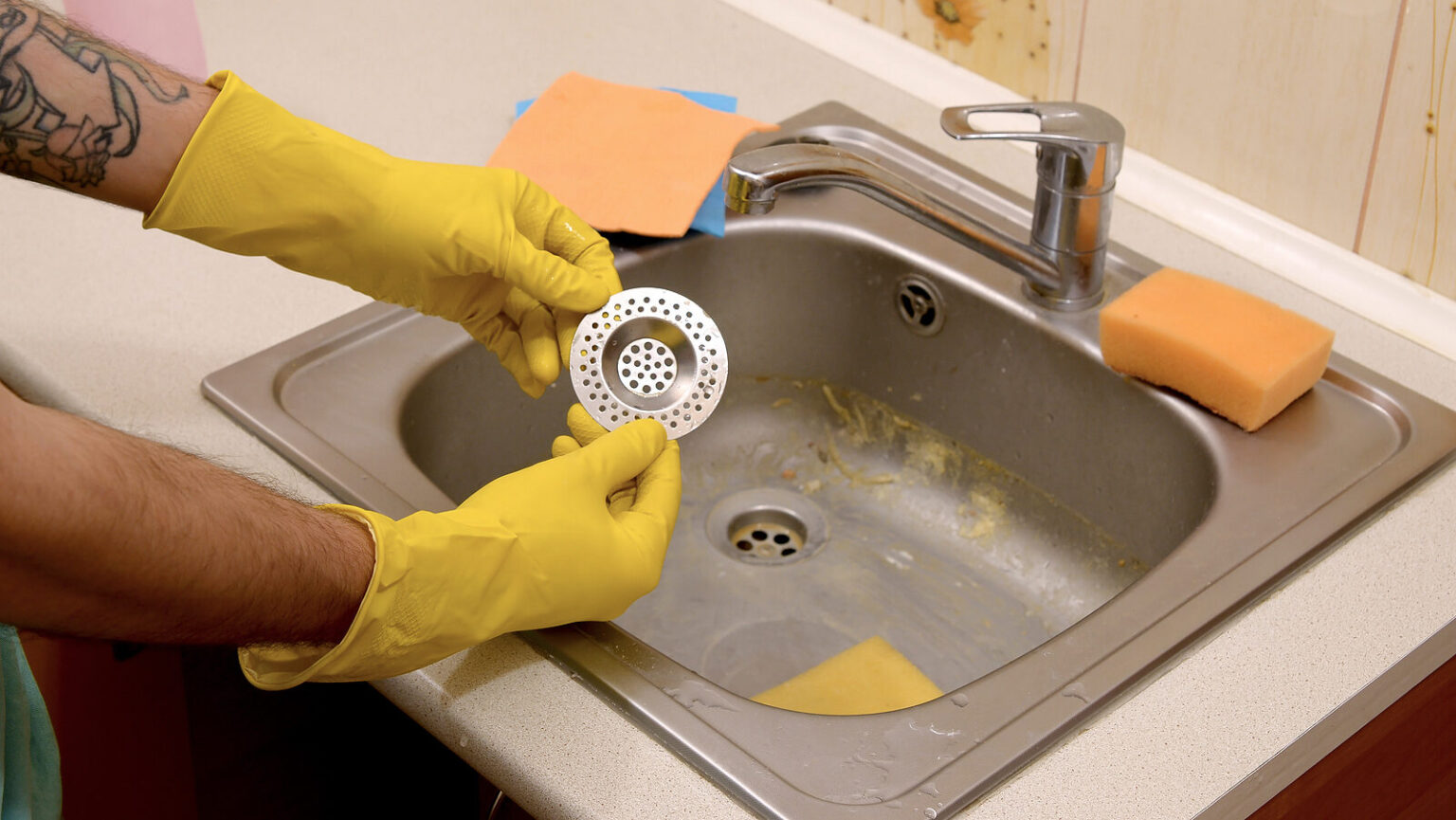 Cleaner In Rubber Gloves Shows Clean Plughole Protector Of A Kitchen Sink Edited 1536x865 
